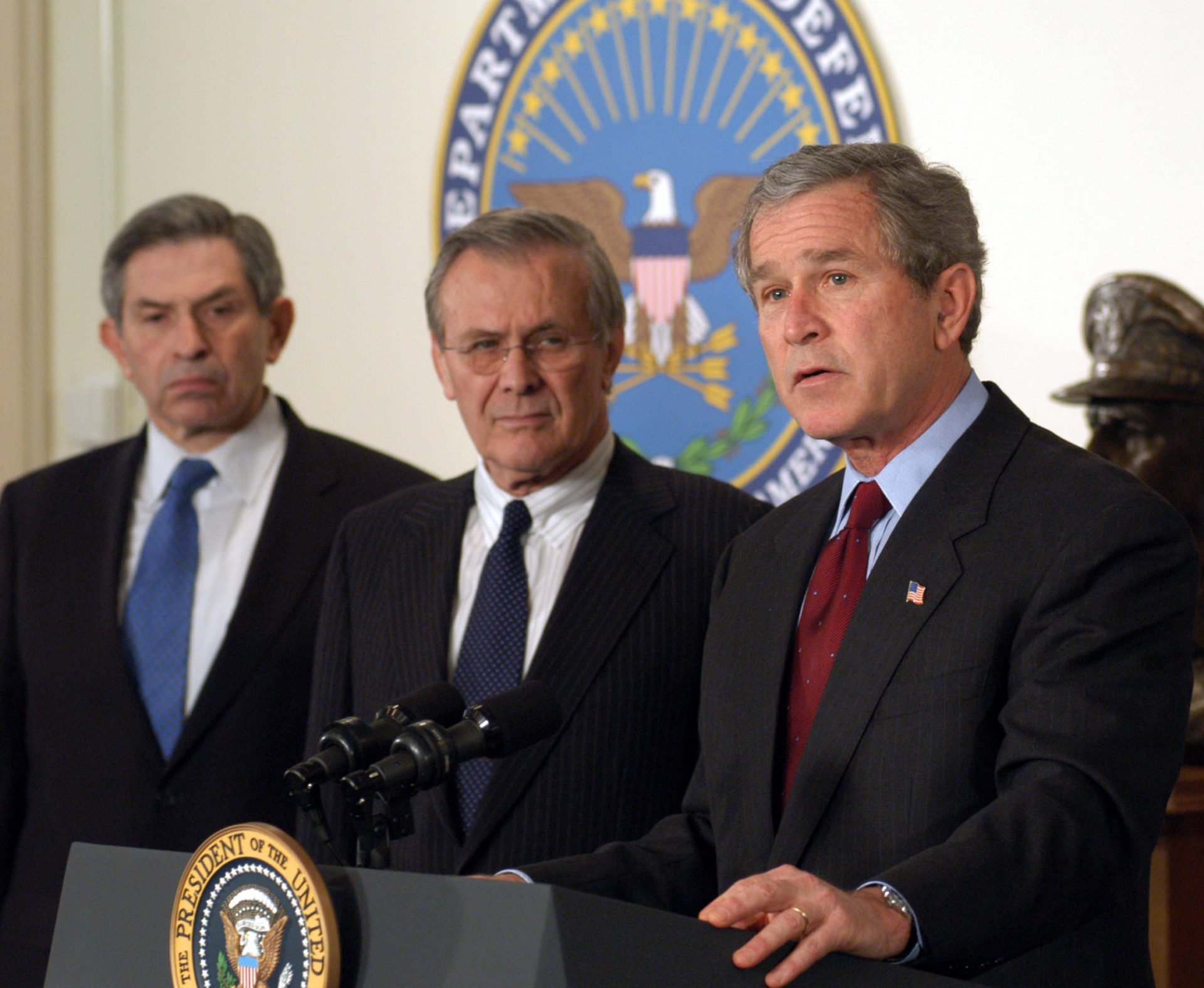 Weitere Einzelheiten Bush mit Verteidigungsminister Donald Rumsfeld (Mitte) und dessen Stellvertreter Paul Wolfowitz 2003, zu Beginn des Irakkriegs | DoD photo by R.D. Ward., Public domain, via Wikimedia Commons